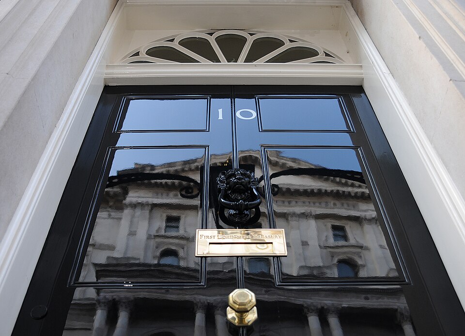 The black front door of 10 Downing Street with its white numeral 10, lion-head knocker and brass letterbox reading First Lord of the Treasury
