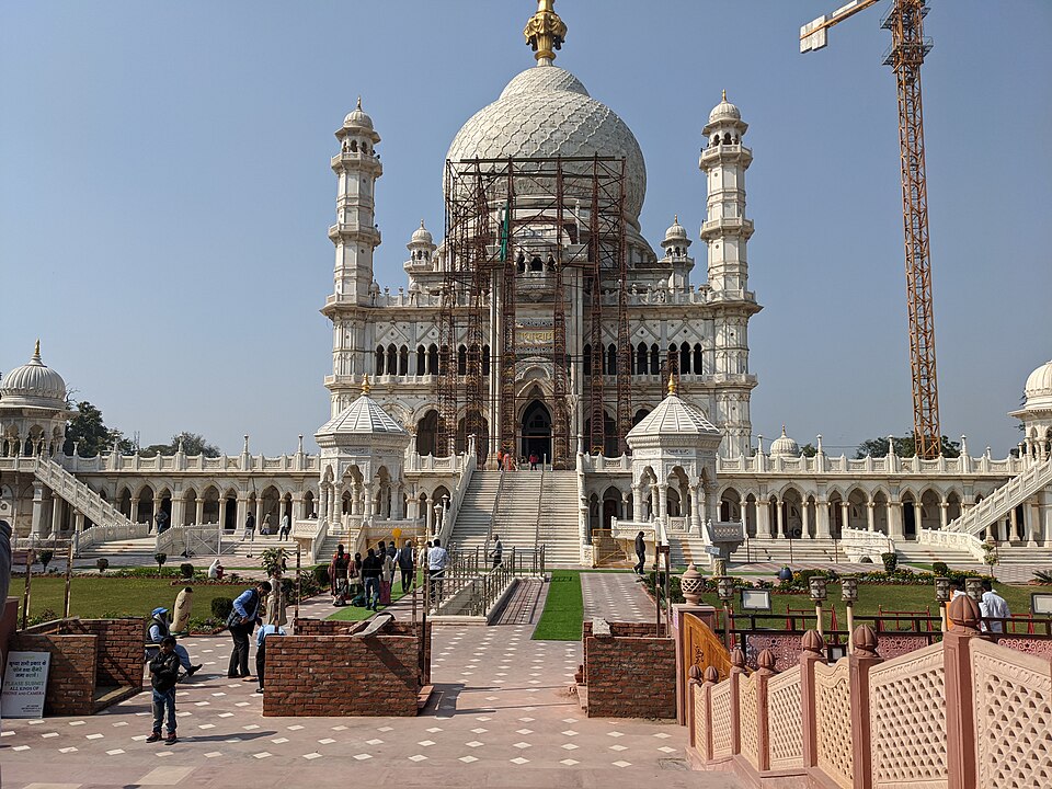 The white marble Radhasoami Samadh at Soami Bagh in Agra, its central dome and corner minarets still partly wrapped in construction scaffolding above a colonnaded terrace