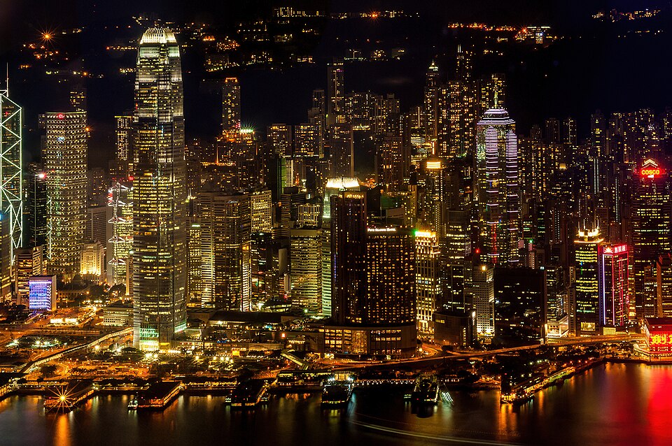 Night view of the densely packed lit office towers of Hong Kong Island rising above the Victoria Harbour waterfront