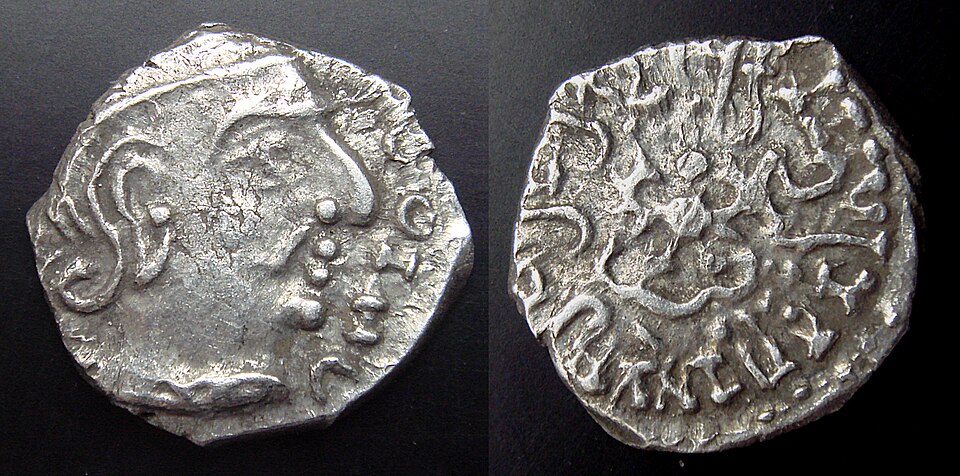 Obverse and reverse of a small worn silver coin: a ruler's bust in profile on one face, a Garuda emblem ringed by a Brahmi legend on the other