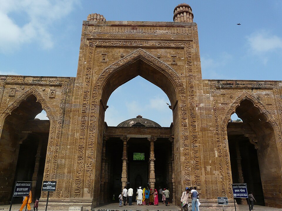 The tall central pointed arch of the carved sandstone screen wall of Adhai Din Ka Jhonpra at Ajmer, framed by bands of Arabic calligraphy, with the pillared prayer hall behind