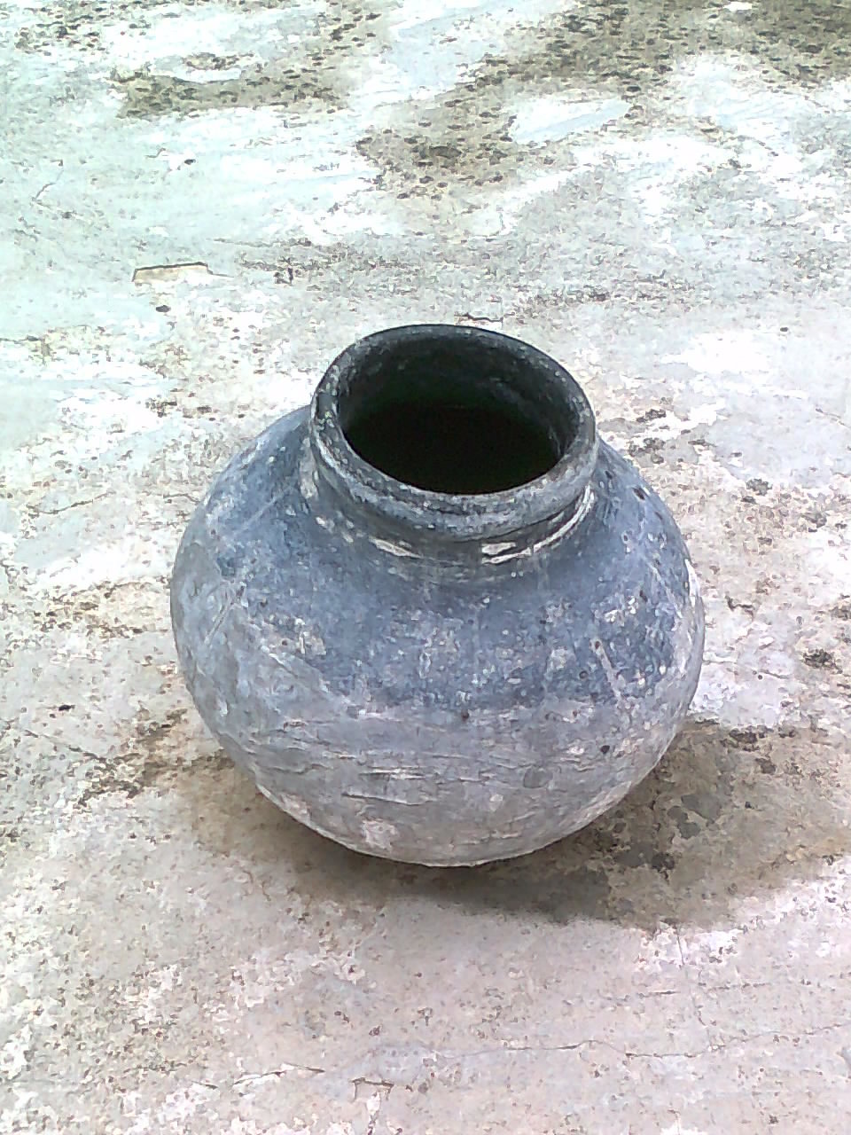 A single round-bellied unglazed clay water pot with a short neck standing on a stone floor