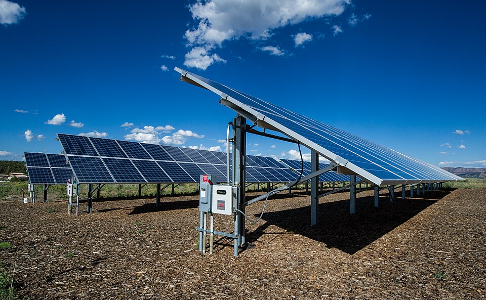 Rows of tilted blue photovoltaic panels on steel frames in an open field under a clear sky