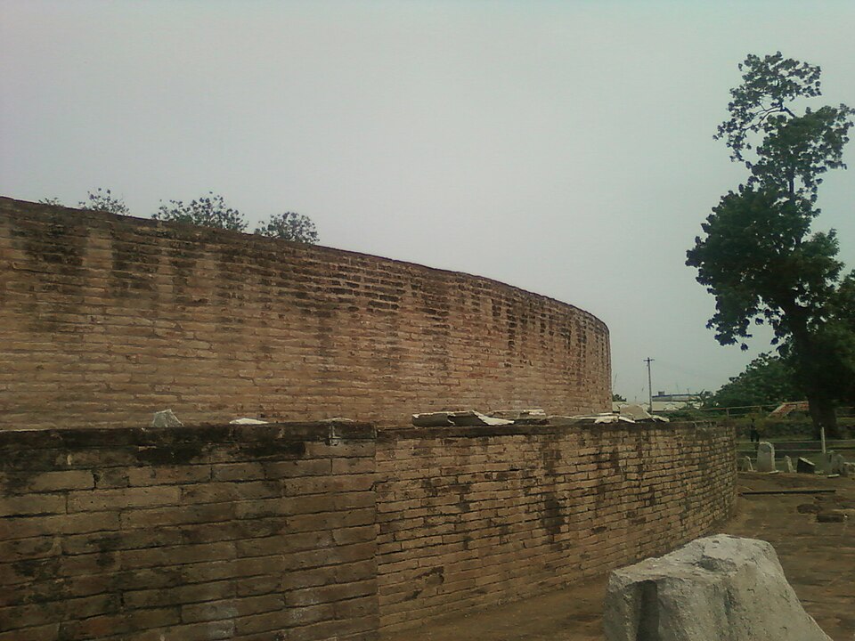 The curved brick drum wall of the ruined Amaravati Mahachaitya stupa, with fallen stone slabs lying on its ledge