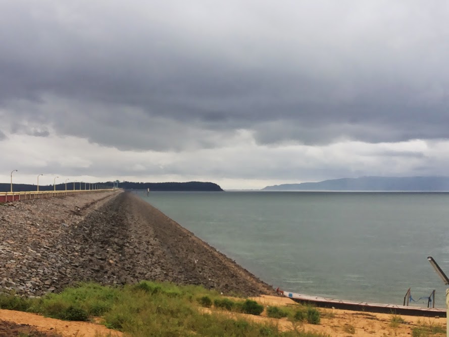 The long stone-faced earthen embankment of the Hirakud Dam curving away beside its wide reservoir on the Mahanadi under a stormy sky