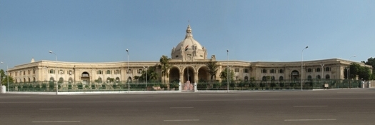 The long sandstone facade of the Uttar Pradesh Vidhan Bhavan in Lucknow, its central dome and pillared portico seen from the road in daylight