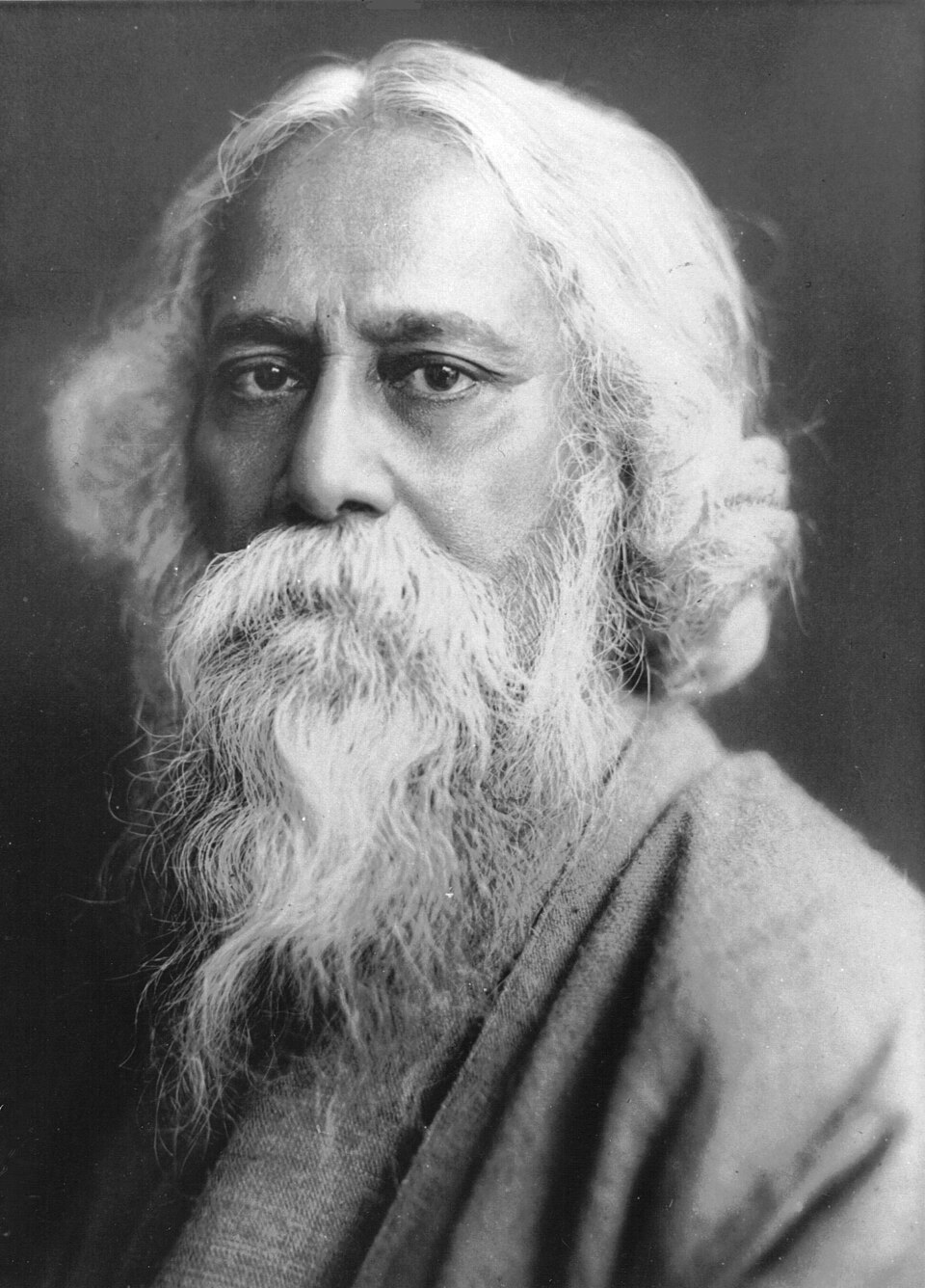 Black-and-white studio portrait of Rabindranath Tagore in later life, with long white hair and flowing beard, wearing a draped robe