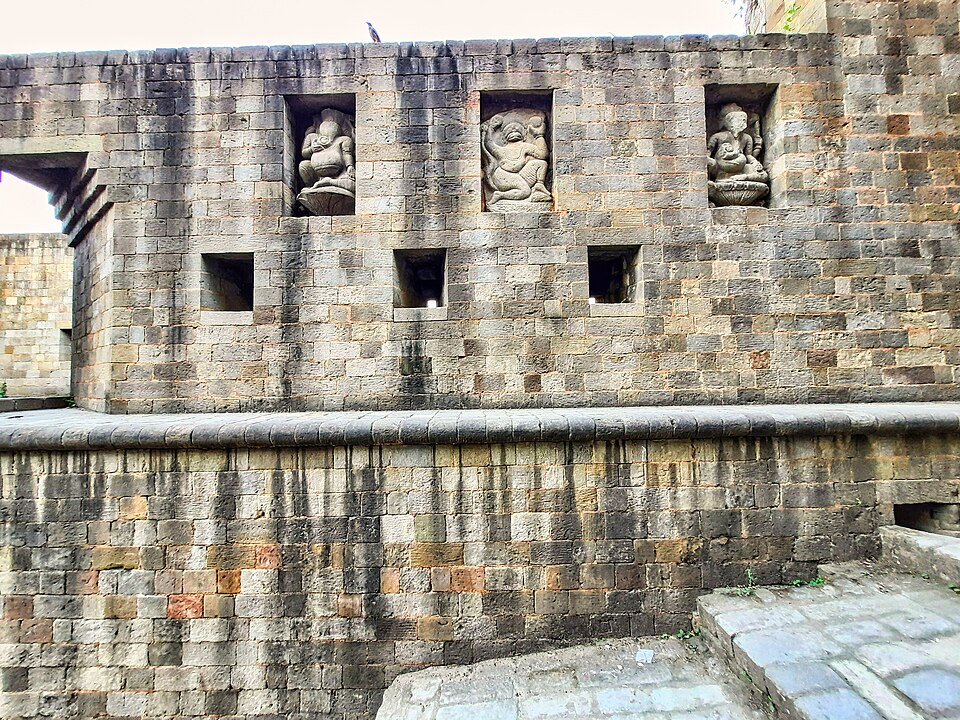 A weathered stone rampart of Kangra Fort in Himachal Pradesh, with carved sculptural figures set in niches along the upper wall