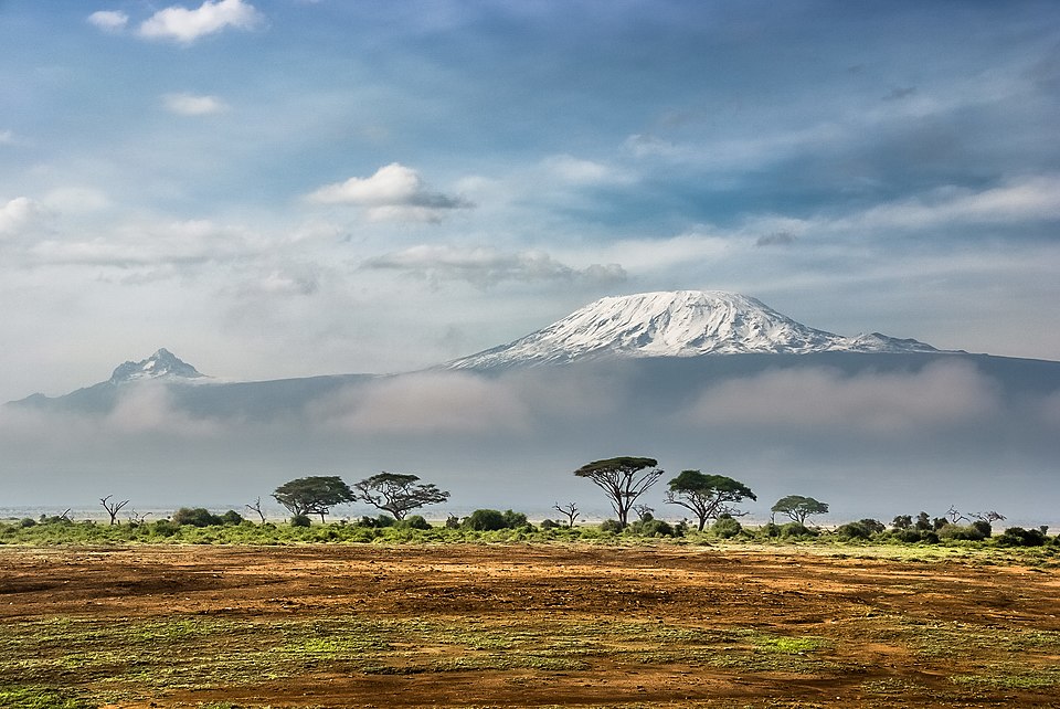 The snow-capped summit of Mount Kilimanjaro rising above the savanna and flat-topped acacia trees, seen from Amboseli