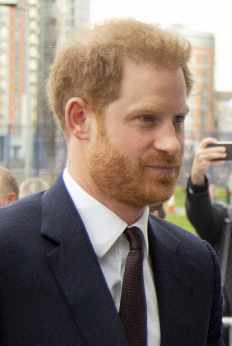 Prince Harry, Duke of Sussex, with red hair and beard in a navy suit and dark tie