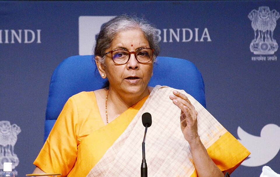 Union Finance Minister Nirmala Sitharaman, in a yellow sari and spectacles, speaking at a government press conference