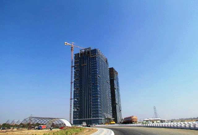 The GIFT One glass office tower rising from open ground at GIFT City near Gandhinagar, Gujarat, with a construction crane alongside