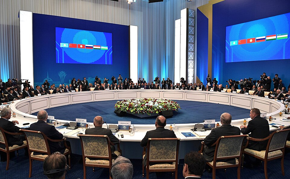 Heads of state seated around a large round table at a Shanghai Cooperation Organisation summit, with member-country flags shown on overhead screens