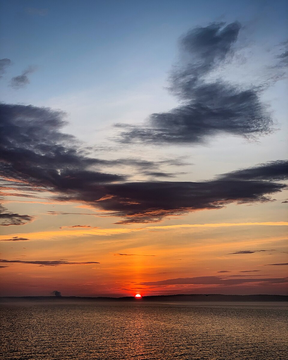 The sun setting over the wide open water of Lake Onega in Karelia, Russia, beneath a partly cloudy sky