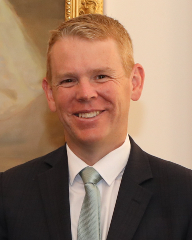 Chris Hipkins, a man with short reddish-blond hair in a dark suit and mint-green tie, smiling