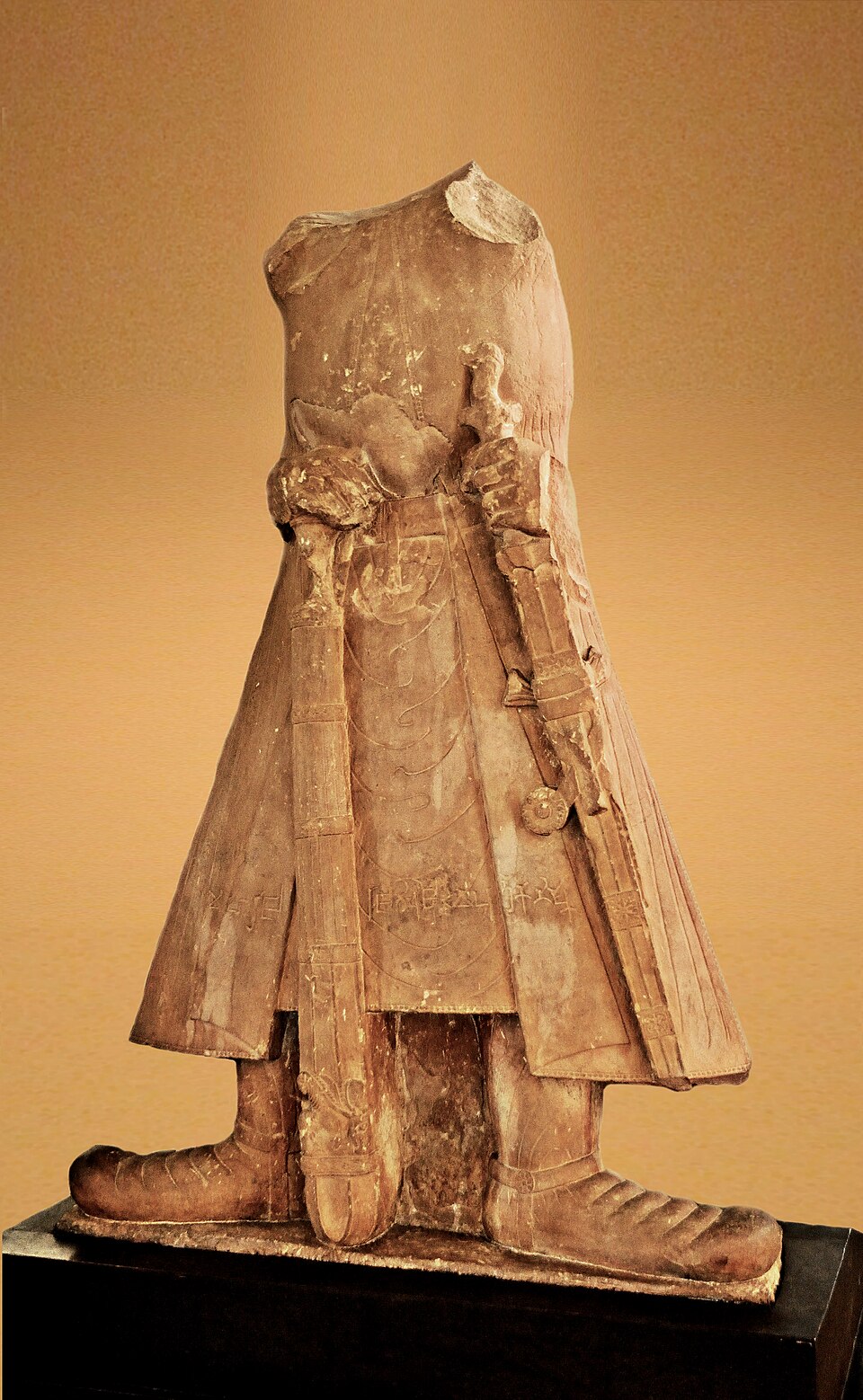 The headless stone statue of Kushan emperor Kanishka I standing in a long belted tunic and heavy boots, grasping a sword hilt
