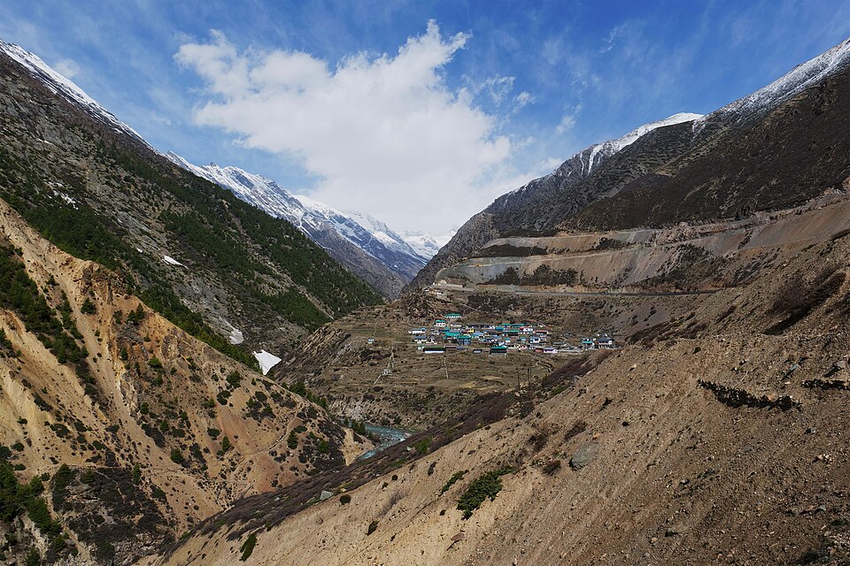 Niti village clustered on a terrace in a high Himalayan valley in Chamoli, Uttarakhand, flanked by barren mountain slopes with snow-capped peaks in the distance