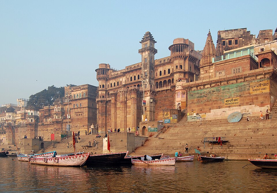 Munshi Ghat on the river Ganga at Varanasi, with ornate riverfront palace buildings above stone steps and wooden boats moored on the water