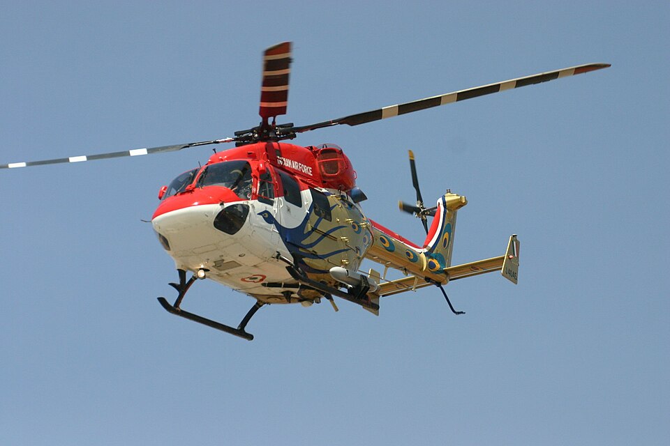 A HAL Dhruv Advanced Light Helicopter in flight against a blue sky, in the red-and-white Indian Air Force Sarang display-team livery marked INDIAN AIR FORCE
