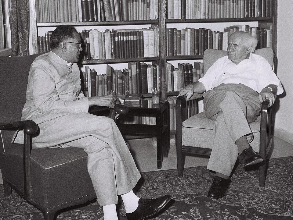 A black-and-white photograph of two men seated in armchairs in a book-lined study: Jayaprakash Narayan on the left in a white Indian kurta and spectacles, talking with the white-haired Israeli Prime Minister David Ben-Gurion on the right