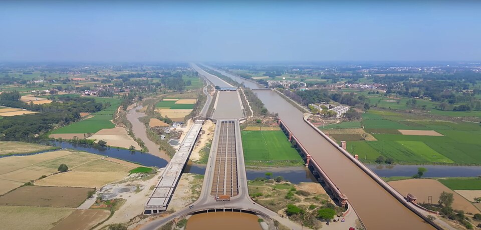 An aerial view of the Upper Ganga Canal at Roorkee running dead straight to the horizon between green and yellow fields, carried across the Solani river on a long red-brick arched aqueduct beside a newer lined channel