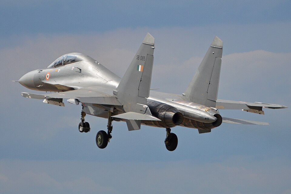 An Indian Air Force Sukhoi Su-30MKI fighter serial SB 065 airborne with its landing gear down, showing the twin engines, twin canted tail fins with the Indian tricolour flash and the roundel on the nose