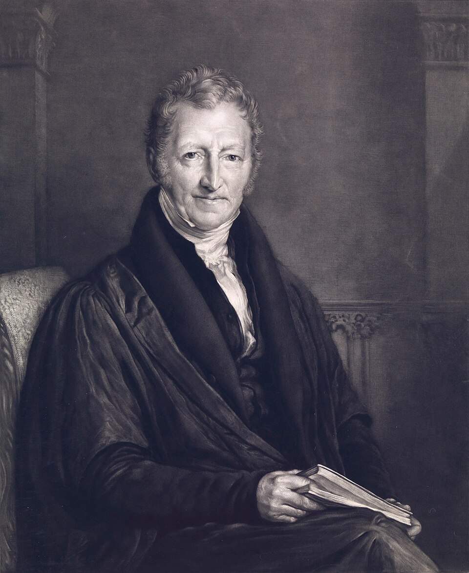 A monochrome portrait of Thomas Robert Malthus seated in a high-backed chair, an elderly man with curling grey hair and long sideburns wearing a dark gown and coat over a white cravat, an open book resting in his hands
