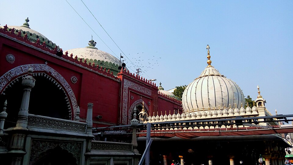 The white ribbed marble dome and gold finial over the tomb of Hazrat Nizamuddin Auliya, seen beside the red sandstone Jamaat Khana mosque with its calligraphic arch, in the Nizamuddin dargah complex in Delhi