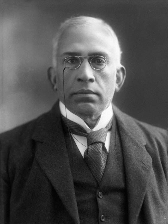 Black-and-white studio portrait of Sir Chettur Sankaran Nair, bald and wearing pince-nez spectacles, a three-piece dark suit and a striped tie