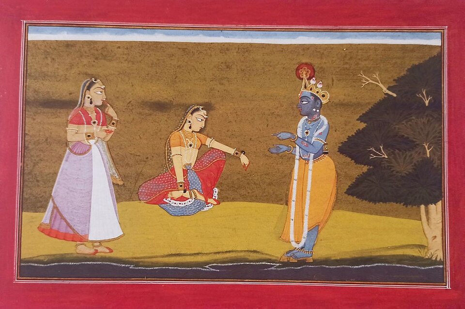 A Pahari miniature painting within a red border showing blue-skinned Krishna in a yellow dhoti gesturing towards Radha, who sits on the ground with a female companion standing beside her