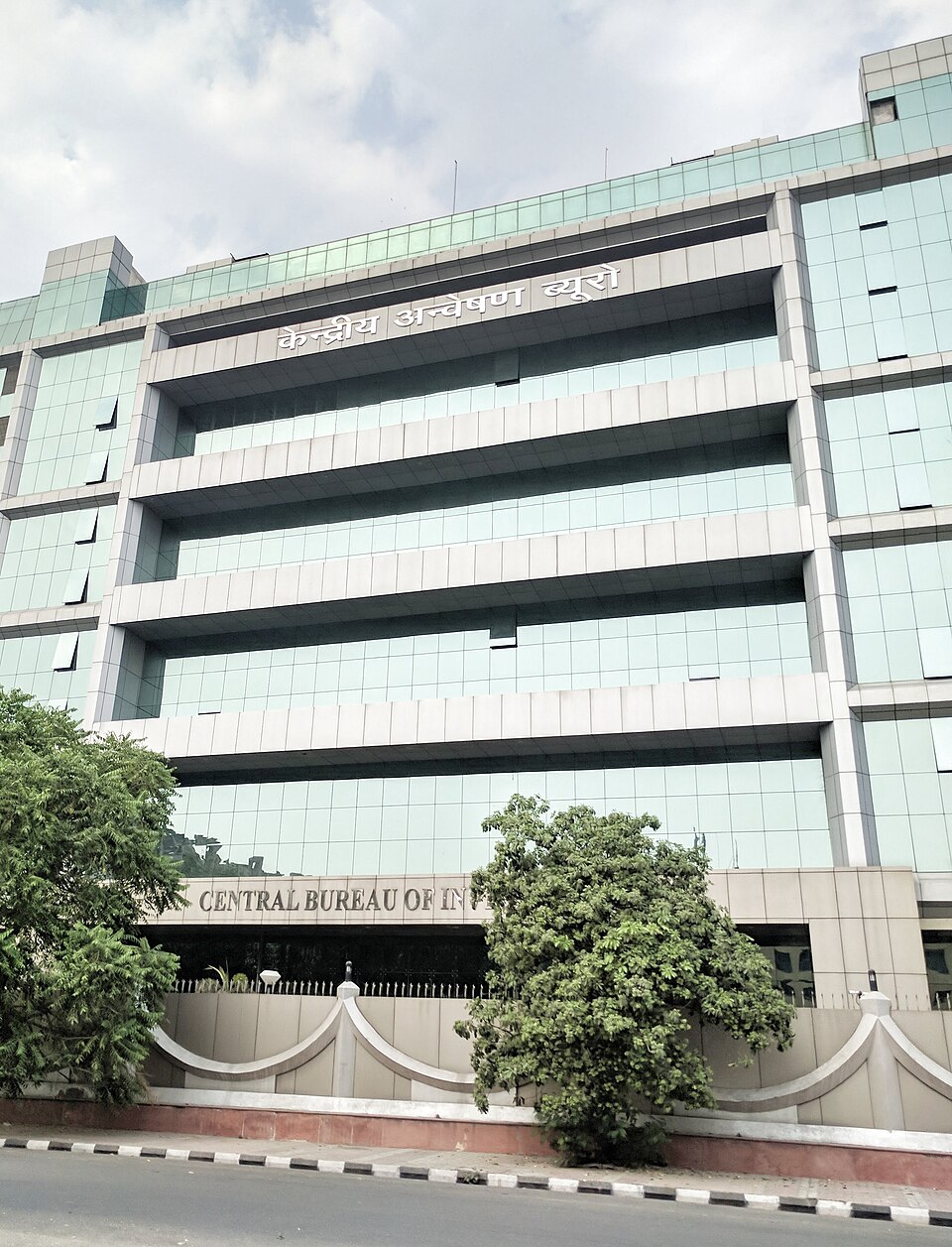 The Central Bureau of Investigation headquarters in New Delhi, a glass-fronted multi-storey building signed 'केन्द्रीय अन्वेषण ब्यूरो' above and 'CENTRAL BUREAU OF INVESTIGATION' at the entrance