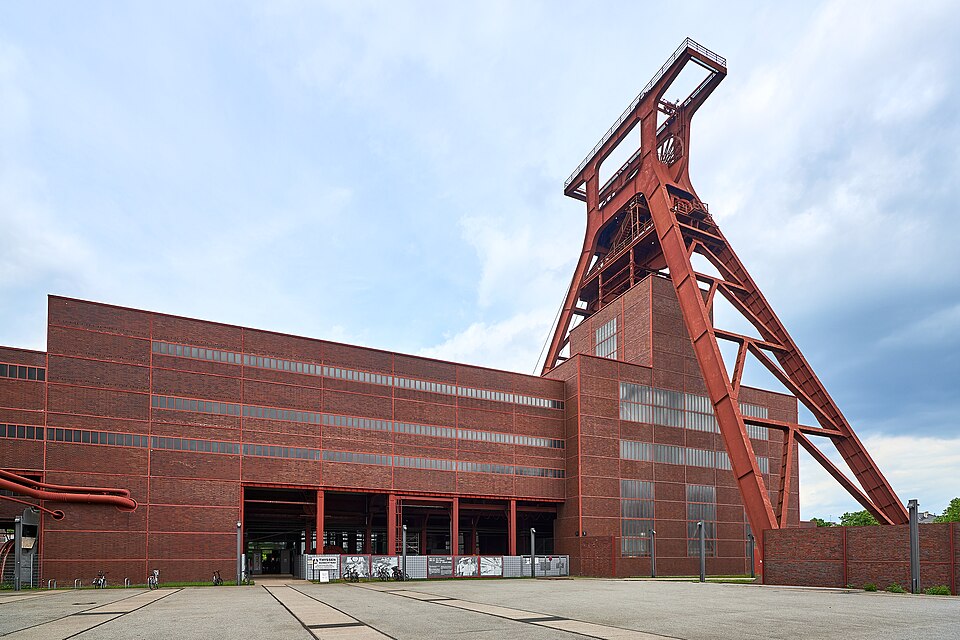 The red steel double-strut winding tower of Shaft XII at the Zollverein colliery in Essen, rising above the long brick pithead building