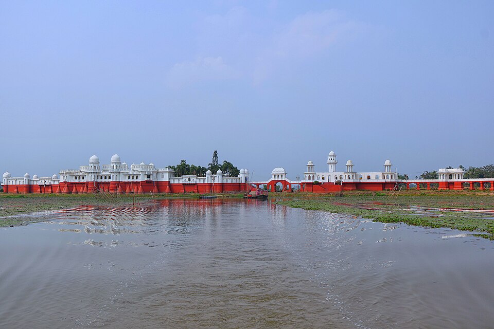 The long red-and-white Neermahal palace seen across the shallow water of Rudrasagar Lake in Tripura, its white domed pavilions and minarets rising above red ramparts